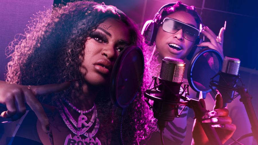 Real Dimez recording vocals into a studio microphone under pink light