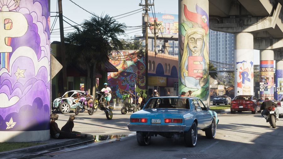 A classic car driving past a colourful mural in a Vice City arts district